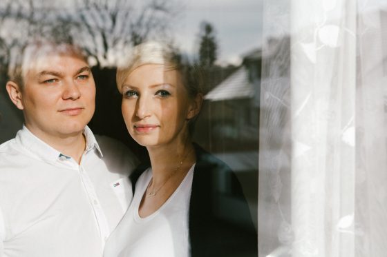 Portret małżeński w oknie z odbiciem otoczenia. Sesja rodzinna i ciążowa w Monachium